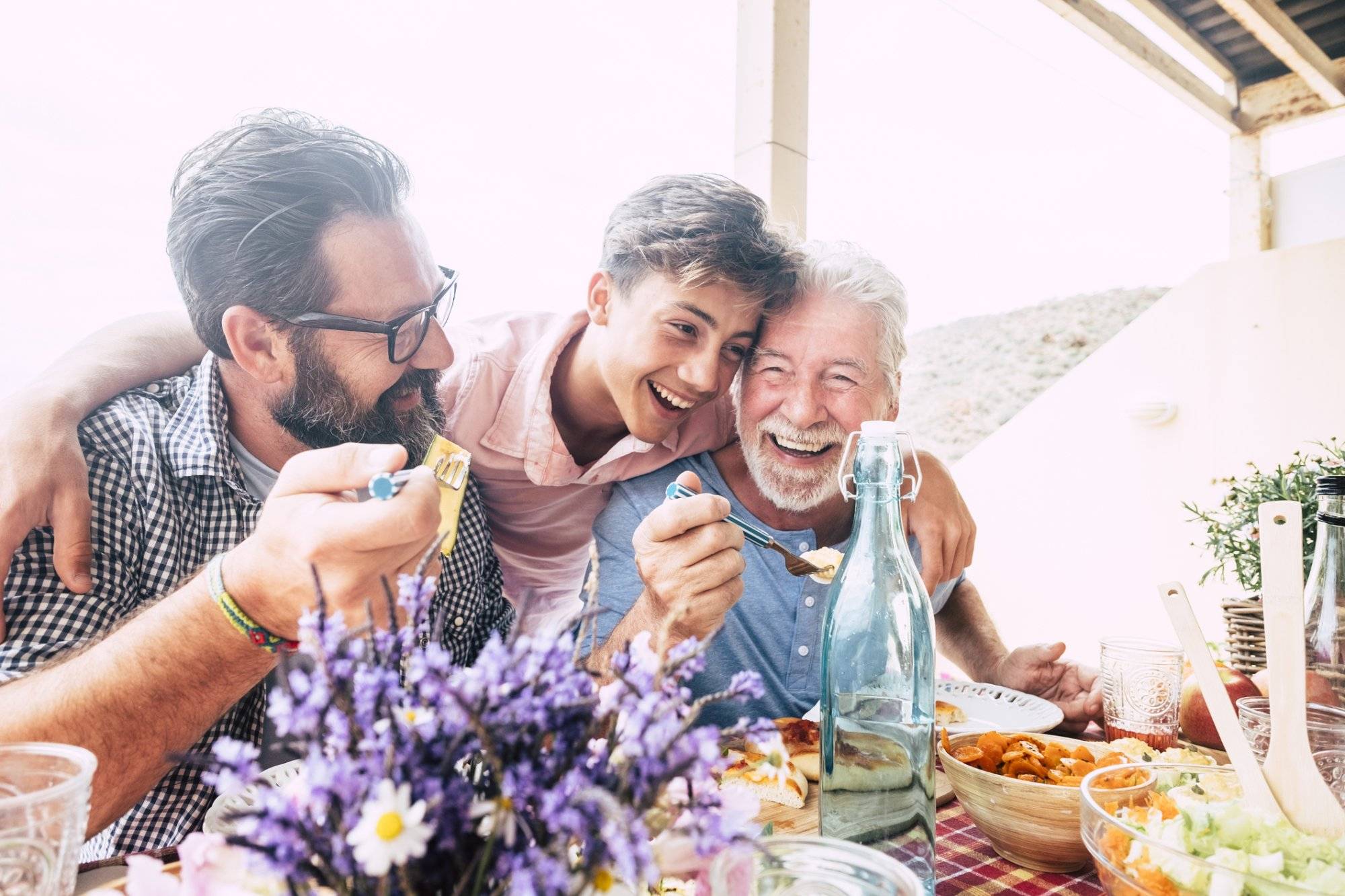 Happy people family concept laugh and have fun together with three different generations ages : grandfather father and young teenager son all together eating at lunch