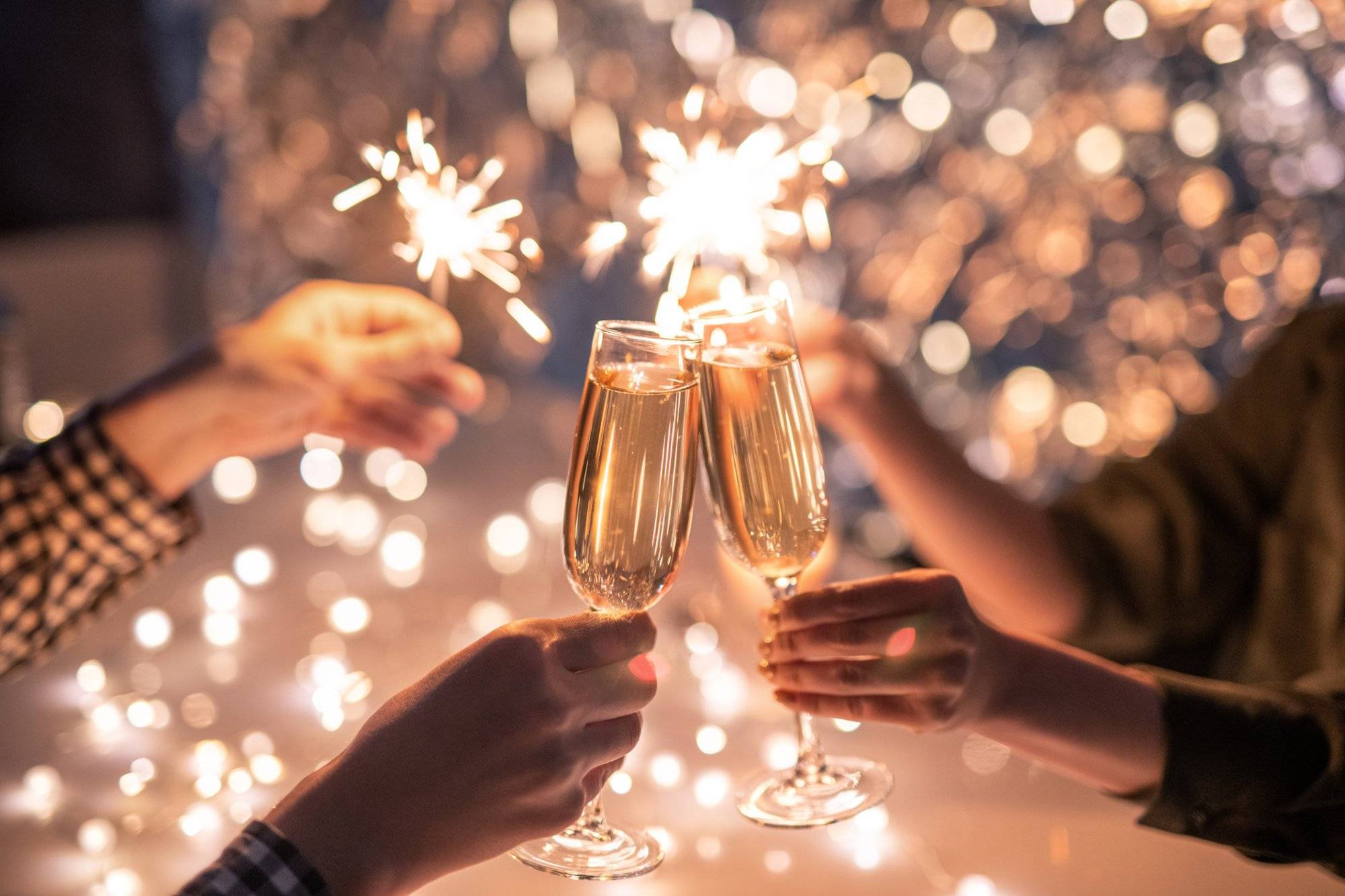 Hands of couple with flutes of champagne and their friends with bengal lights Hands of couple with flutes of champagne and their friends with bengal lights