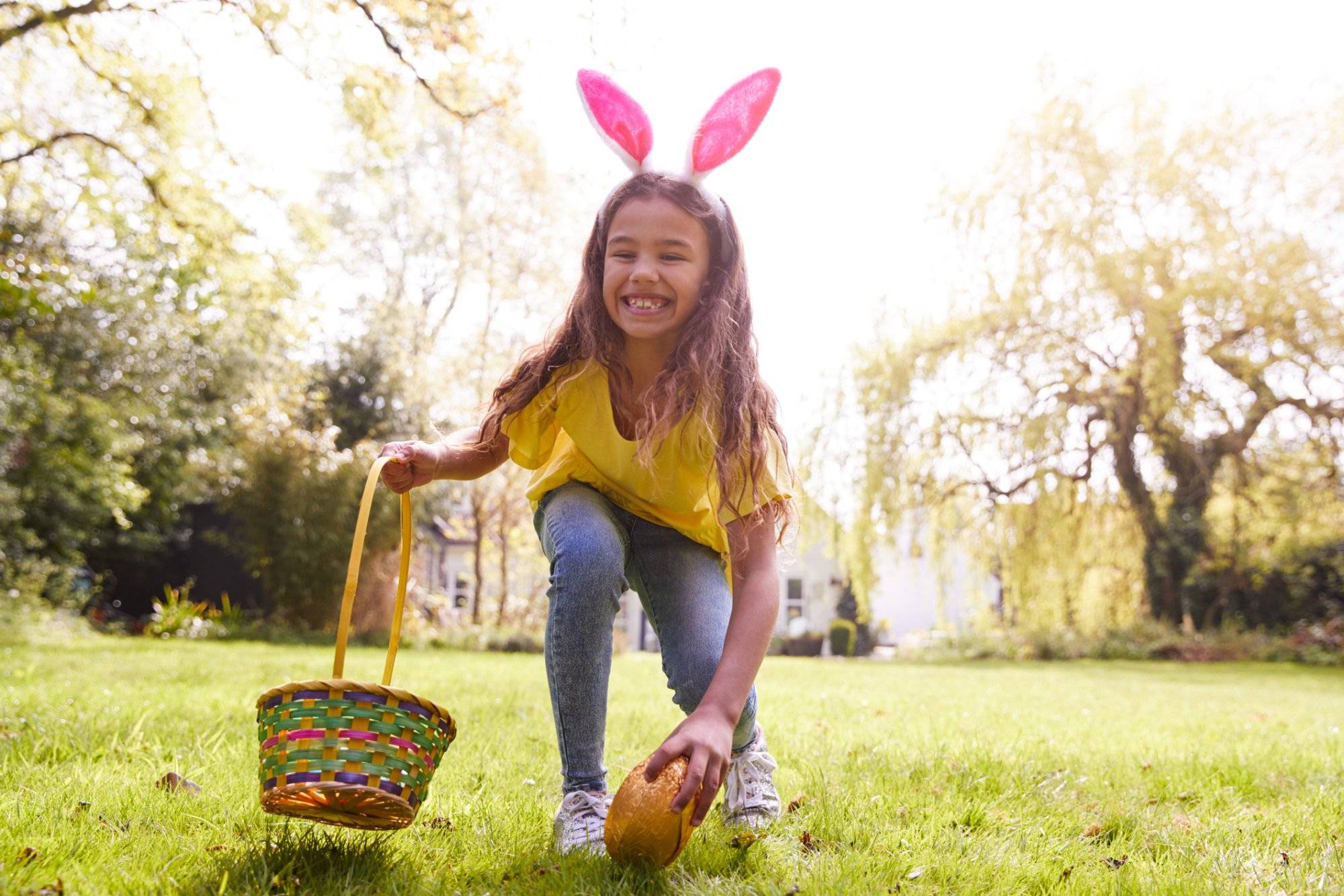 Portrait Of Girl Wearing Bunny Ears Finding Chocolate Egg On Easter Egg Hunt In Garden Portrait Of Girl Wearing Bunny Ears Finding Chocolate Egg On Easter Egg Hunt In Garden