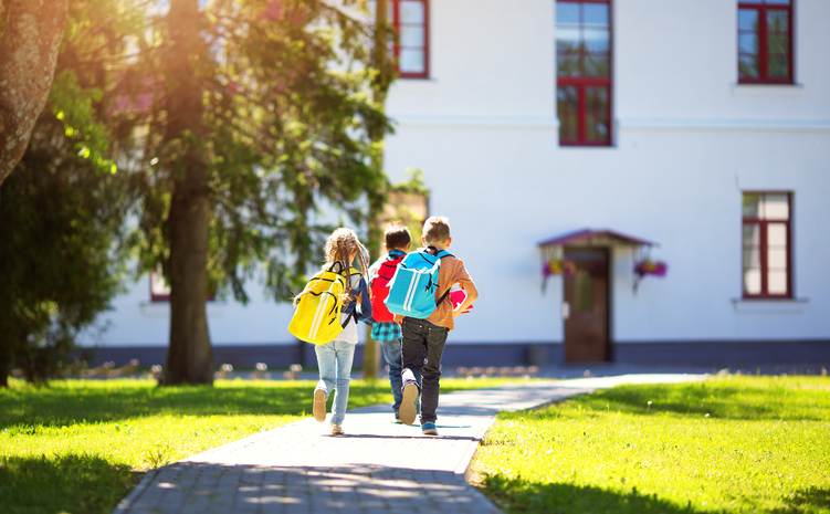 Children with rucksacks running in the park near school